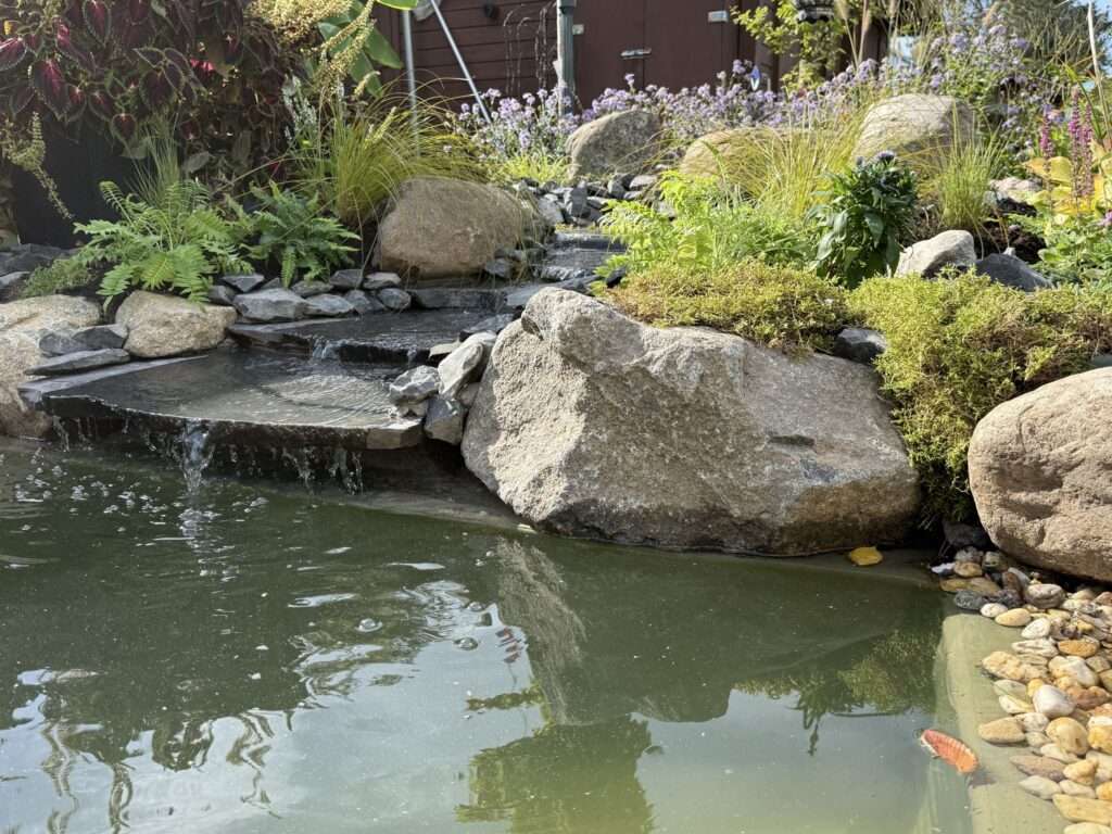Einlauf des Bachlaufs: Wasser fließt über eine Natursteinplatte in den Teich